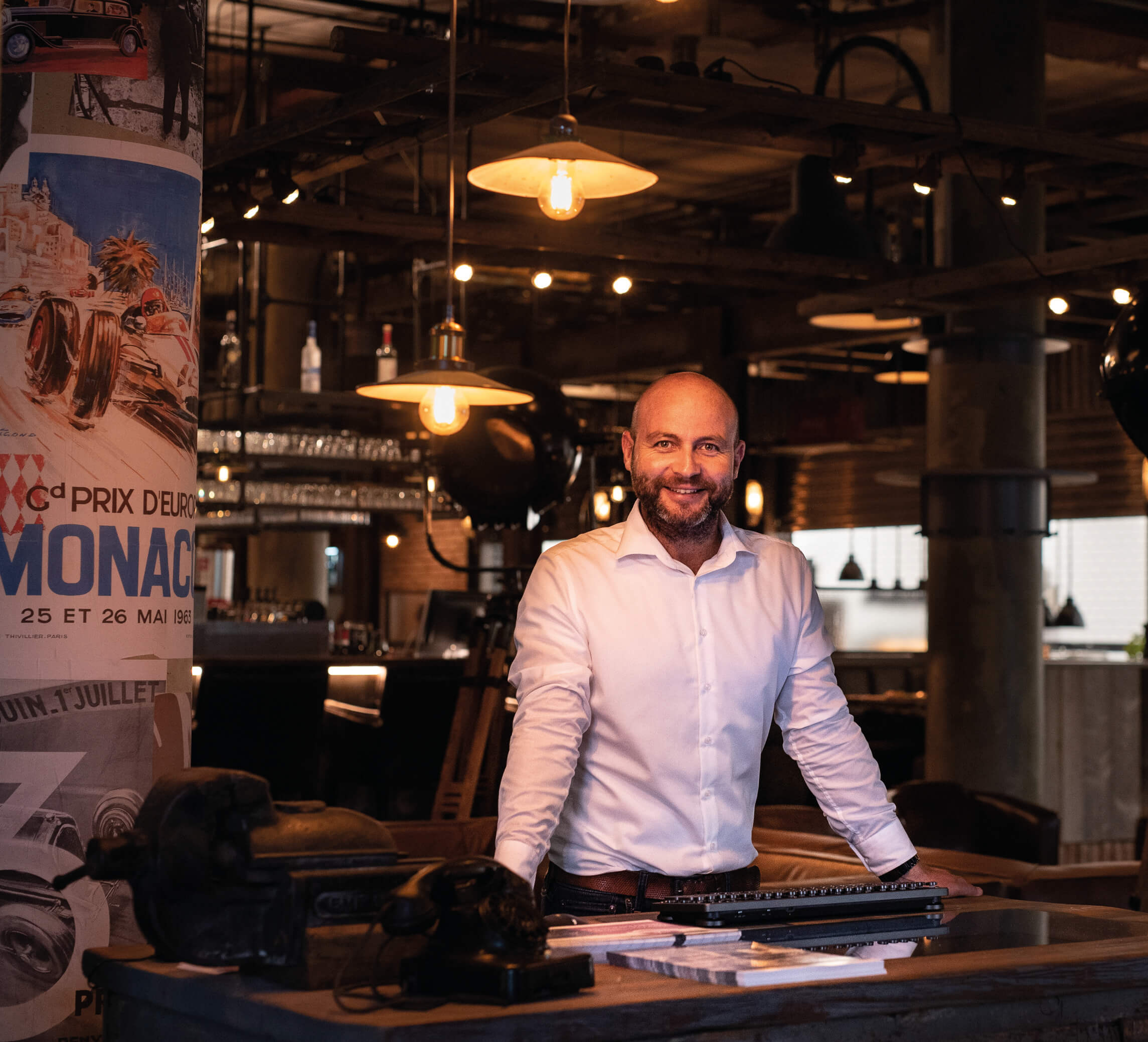 Smiling man in white shirt behind bar counter, industrial ambience