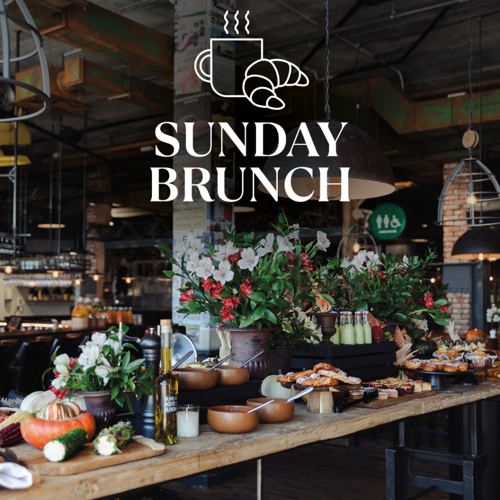 Breakfast or brunch buffet with flower arrangements, bread, pastries, vegetables, oil bottles and cups in a rustic function room.